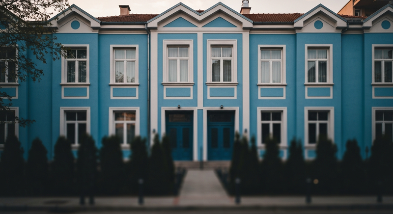Symmetric golden hour photograph of the blue townhouse exterior of Made in Blue, Sofia, Bulgaria — minimal architectural composition, 35mm film look, soft warm light on painted plaster and stone steps